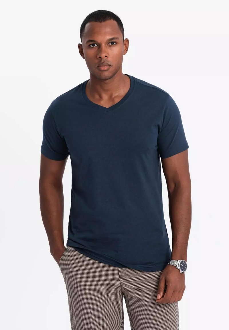 Navyblaues V-Ausschnitt-T-Shirt aus weichem Stoff, mit kurzen Ärmeln und bequemer Passform. Kombiniert mit karierter Hose und einer silbernen Uhr.