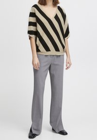 Beżowy i czarny sweter z oversize'owym krojem z dekoltem w kształcie litery V, zestawiony z jasnoszarymi, dopasowanymi spodniami i czarnymi butami na szpilkach.