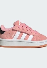 Ružové semišové tenisky s bielymi tromi pruhmi, gumovou podrážkou, textúrovanými akcentmi a ružovými šnúrkami. Obsahujú čierny pätový tab a perforácie.