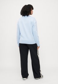Hellblaues Sweatshirt mit lockerem Schnitt und gerippten Bündchen, kombiniert mit schwarzen, weiten Hosen, die an den Seiten einen cremefarbenen Streifen haben.