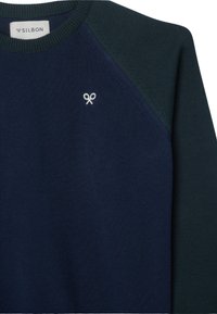 Jersey azul marino con mangas raglán en verde oscuro, hecho de tela de punto. Presenta un pequeño logo blanco cerca del escote.