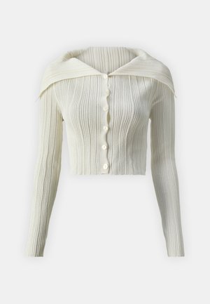 Cardigan bianco a coste con colletto classico, maniche lunghe e sei bottoni sul davanti. Texture morbida e design corto aderente.