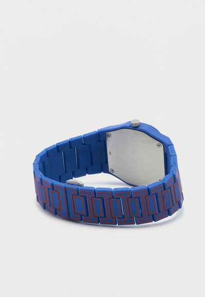 Μπλε λουράκι ρολογιού με κόκκινα γεωμετρικά σχέδια, προσαρτημένο σε ασημένιο πίσω μέρος ρολογιού με τέσσερις βίδες και κορώνα στο πλάι.