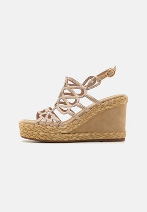 Sandalia de cuña con un upper de ante sintético beige, tiras cruzadas ornamentadas y una plataforma de yute trenzado. Cuenta con un hebilla ajustable en el tobillo.