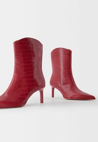 Red, croc-embossed ankle boots with pointed toes and thin, stiletto heels. Smooth texture, above-ankle height, minimalistic design.