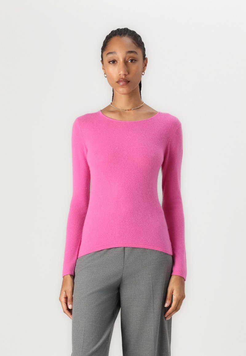 Rosa, langärmliger Pullover aus weichem Strickmaterial mit rundem Ausschnitt und schmaler Silhouette, kombiniert mit grauen Hosen.