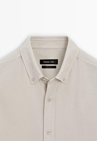 Camicia button-up beige chiaro con collo classico, caratterizzata da una patta anteriore pulita e dettagli cuciti. Etichetta con la scritta "Massimo Dutti."