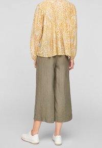 Blusa floreale gialla con dettagli arricciati sul retro, abbinata a pantaloni larghi in lino beige e sneakers bianche.