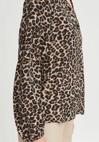 Leopardenmuster Bluse in einer Mischung aus Schwarz, Braun und Beige, lockere Passform, elastische Bündchen und ein V-Ausschnitt.