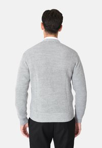 Maglione grigio a costine con una texture a maglia, scollo rotondo e maniche lunghe, abbinato a pantaloni neri, mostrato da dietro.
