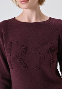 Maglione bordeaux con scollatura a costine e lettere testurizzate "R" e "R" sul davanti. Realizzato in tessuto morbido, presenta un design aderente.