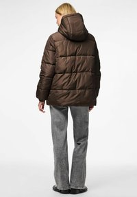 Chaqueta acolchada marrón con capucha, con un diseño acolchado, textura brillante y puños elásticos. Llevada sobre unos vaqueros rectos grises.