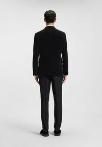 Zwarte fluwelen blazer met een klassieke snit, voorzien van een soepele textuur en een op maat gemaakte pasvorm, gecombineerd met zwarte broeken en schoenen.