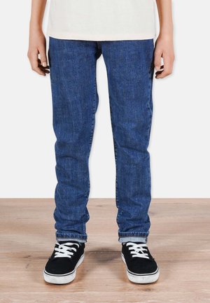 Sinisiä farkkujeansseja, joissa on slim fit -malli, haalistunut tekstuuri ja perinteinen viisi-taskumalli, yhdistettynä mustiin nauhakenkiin.