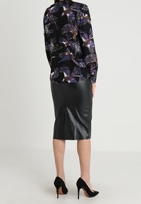 Svart blommig blus med lång ärm och mönster av flerfärgade fåglar och solfjädrar, kombinerad med en figursydd svart läderpennkjol och svarta stilettklackar.