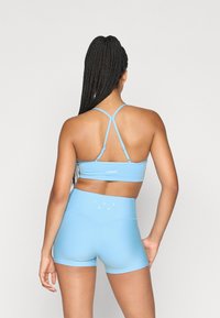 Ανοιχτό μπλε φανελάκι γυμναστικής με εφαρμογή και ψηλόμεσα σορτς από ελαστικό ύφασμα, διαθέτοντας λεπτές σταυρωτές τιράντες και διακριτική σήμανση στην πλάτη.