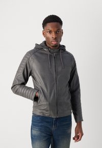 Graue Lederjacke mit Kapuze, ausgestattet mit gesteppten Schulterdetails, zwei Reißverschlusstaschen und einer taillierten Passform. Trägt man über Jeans.