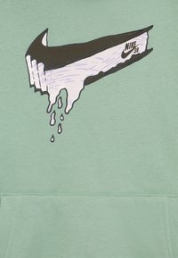 Felpa in cotone verde con un grande logo Nike in bianco e nero con effetto goccia, posizionato centralmente sulla parte anteriore.
