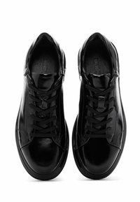 Zapatillas de charol negro con puntera redondeada, cordones planos y un diseño limpio. Acentos texturizados a lo largo de los lados.