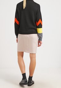 SchwarzerStrickpullover mit orangefarbenen und gelben Zickzackmustern an den Ärmeln, kombiniert mit einem figurschmeichelnden beigen Rock; getragen mit schwarzen Knöchelstiefeln.