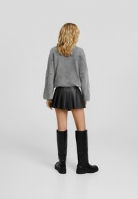 Grauer übergroßer Pullover, schwarzer plissierter Minirock und kniehohe schwarze Stiefel. Glatte Textur, lockere Passform und geschichtete Designdetails.