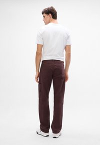 Pantaloni cargo bordeaux con vestibilità dritta, due tasche laterali e tessuto strutturato, abbinati a una t-shirt bianca semplice a girocollo.