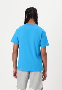 Modra bombažna majica s kratkimi rokavi in krožnim izrezom, oblečena z sivimi kratkimi hlačami; vidne pletenice na zadnjem delu glave.