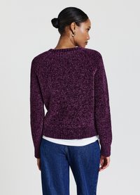 Lila gestrickter Pullover mit strukturiertem Finish, geripptem Saum und Bündchen, mit Rundhalsausschnitt und Raglanärmeln, getragen über einem weißen Oberteil.