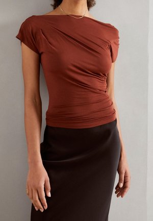 Haut ajusté marron avec des détails drapés, manches courtes et une texture lisse, associé à une jupe en satin noire. Accent d'un collier simple.