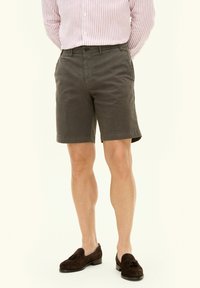 Pantaloni corti grigi da uomo in cotone con frontale piatto, tasche laterali e orlo appena sopra il ginocchio, abbinati a mocassini marroni.