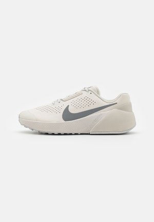 Jasnobeżowy but do biegania Nike z szarym logo swoosh, perforowaną cholewką i grubą miękką podeszwą, widoczny z boku na białym tle.