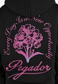 Felpa nera con cappuccio caratterizzata da una grande stampa floreale rosa e testo che recita "Ogni giorno è una nuova opportunità" e "Pegador" in lettering stilizzato.