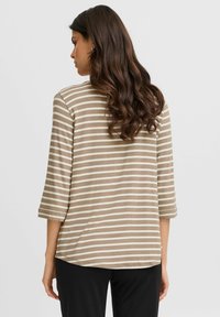 Maglietta a maniche lunghe beige e crema a righe con orlo arrotondato e maniche a tre quarti, realizzata in tessuto morbido. Sono visibili anche pantaloni neri.