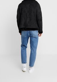 Mustat mokkajakku, jossa on pehmeä kaulus, yhdistettynä vaaleansinisiin farkkuihin. Valkoiset tennarit jaloissa täydentävät rentoa ilmettä.