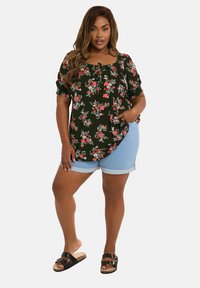 Svart blommig blus med korta ärmar, med röda och gröna mönster, kombinerad med ljusblå denimshorts och svarta sandaler.