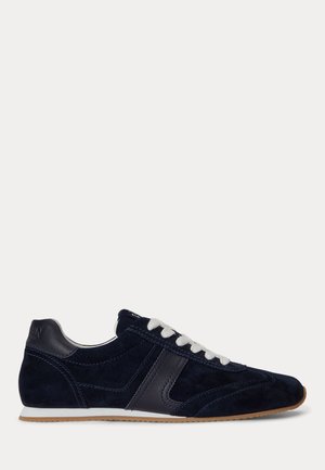 Zapatilla deportiva de ante y piel azul marino con cordones blancos y suela de goma, mostrada de perfil sobre fondo blanco.