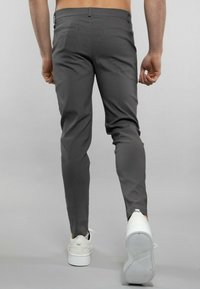 Pantalons gris ajustés avec une texture lisse et une taille plate, dotés de poches arrière et de baskets blanches à semelles épaisses.