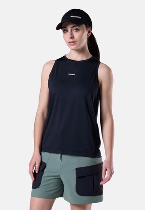 Vrouw die een zwart mouwloos topje en een pet met het Rossignol-logo draagt, olijfgroene korte broek met grote zwarte zakken, staand tegen een witte achtergrond.