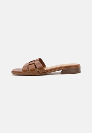 Brun læder flad slip-sandal med flettede remme og lav stabelhæl set fra siden på hvid baggrund.