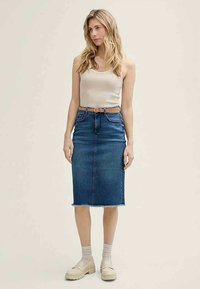 Jeansová tužková sukně v tmavě modré barvě s roztrhaným lemem, doplněná béžovým tílkem a hnědým páskem, nošená s světlými platformovými botami.