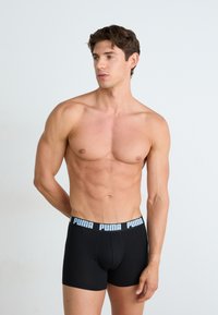 Boxeri negri dintr-un material elastic, cu o talie lată din elastic, purtând logo-ul PUMA în alb pe un fundal negru.