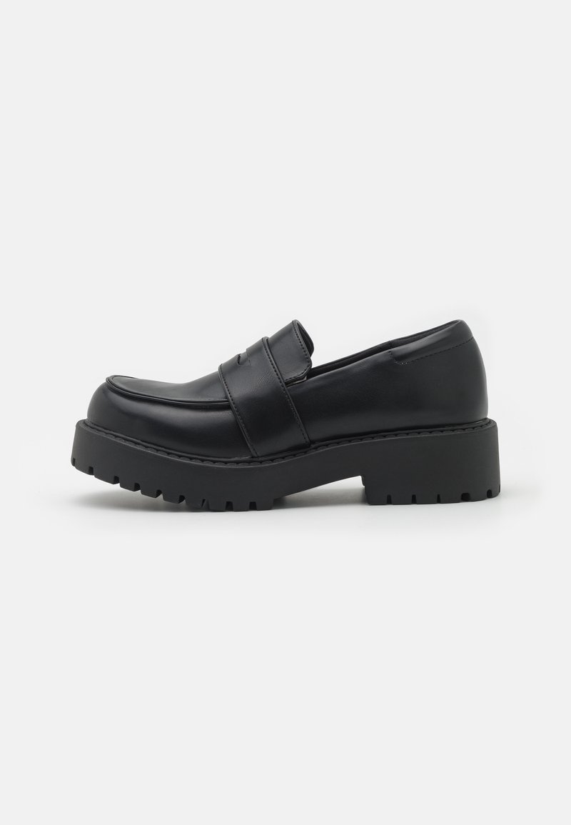 Mocassin en cuir noir avec une semelle épaisse à crampons et un détail de sangle, présenté de profil sur fond blanc.