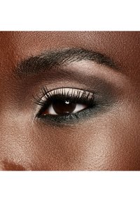 Primer plano de un ojo marrón con pestañas definidas, delineador oscuro y una sombra de ojos neutra que se mezcla en una textura de piel suave y rica.
