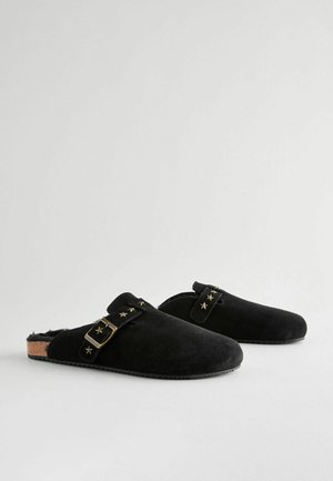 Čierne semišové dreváky s korkovou podrážkou, so strapcom s hviezdičkovými akcentmi a mosadznou sponou. Hladký povrch a uzavretý dizajn na päte.