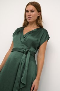 Green wrap dress made of smooth fabric, featuring a V-neck, short sleeves, and a tied waist sash. Textured surface with a subtle sheen.