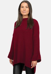 Pull en tricot bordeaux avec un col montant, une texture côtelée et des manches longues évasées ; il présente un ourlet légèrement incurvé et une coupe décontractée.