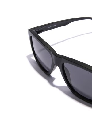 Ochelari de soare negri cu un finisaj mat, formă rectangulară și lentile întunecate. Marcați "Fabricat în Spania" pe brațul interior.