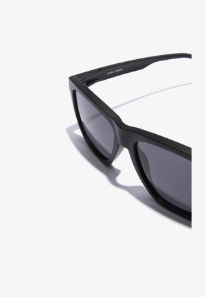 Gafas de sol negras con acabado mate, forma rectangular y lentes oscurecidos. Marcadas "Hecho en España" en el interior de la patilla.