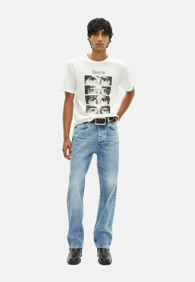 Witte graphic t-shirt met zwarte foto's, gecombineerd met lichtblauwe spijkerbroek. Een zwarte riem en glanzende zwarte schoenen maken de outfit compleet.