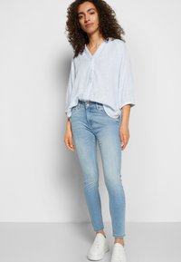 Camisa de botão às riscas azul claro, corte solto, combinada com jeans skinny azul claro e sapatilhas brancas. Tecido suave e design casual.